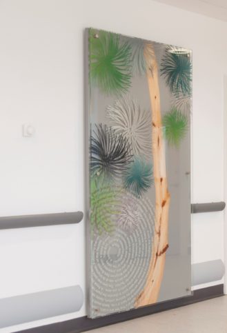 A grey artwork panel which contains a slice of branch from the famous 'Eisenhower' tree along with a white swirl of interpretive text and blue, green and white pine needle swirls by artist Chris Tipping