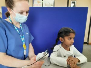 A child with an earphone in one of her ears while nurse looks at the meaurements