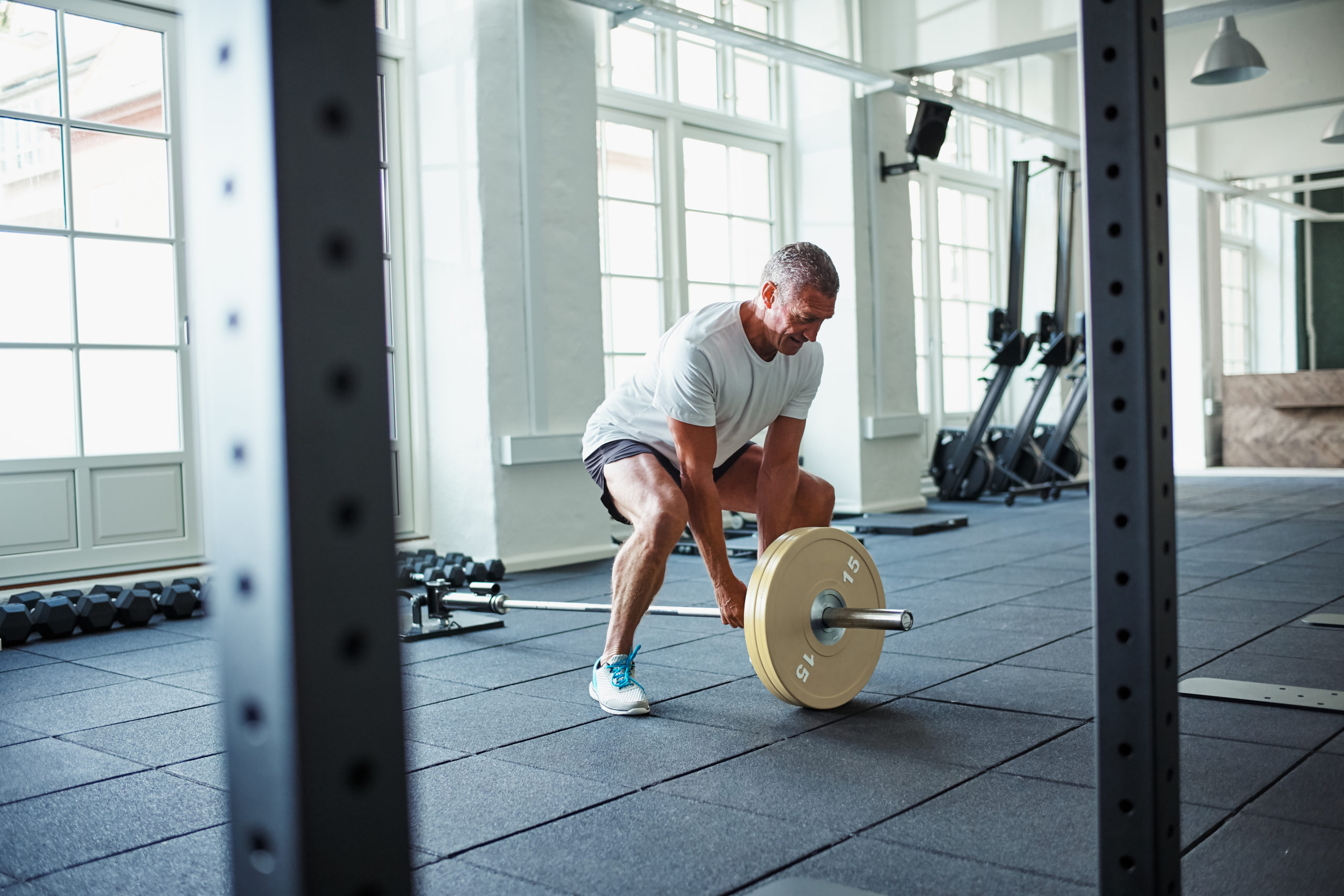 Focused senior man in sportswear standing alone in a gym lifting weights during a workout