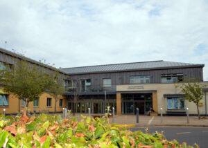 An image of the front of South Petherton Hospital. The building ground floor is yellow with a off white entrance. The first floor is covered in slotted wood cladding.