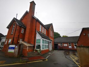 Wellington hospital is a old red brick style house hospital. It is two stories high with extended pitched parts of the house with a very tall chimney breast. There is a very small parking area and behind that is another but much newer one story building in the same style red brick with pitched roof.