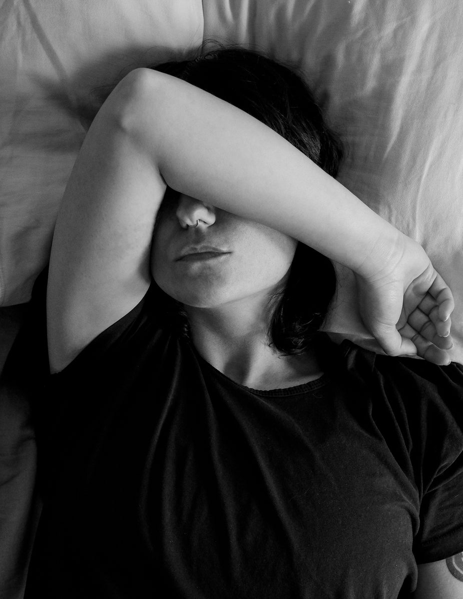 Black and white photograph of a person laid in bed covering their face.