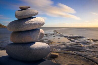 a tower of 5 stones on the beach with a blue sky and the sea in the background