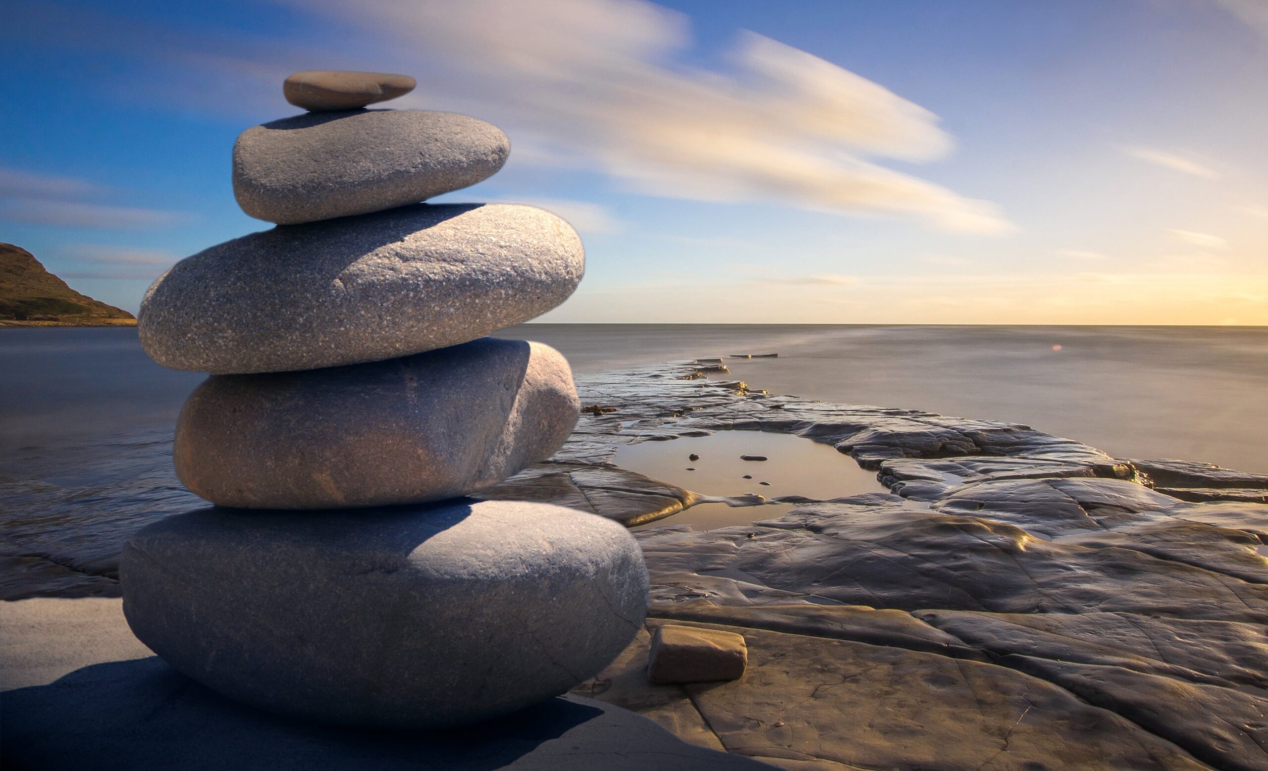 a tower of 5 stones on the beach with a blue sky and the sea in the background