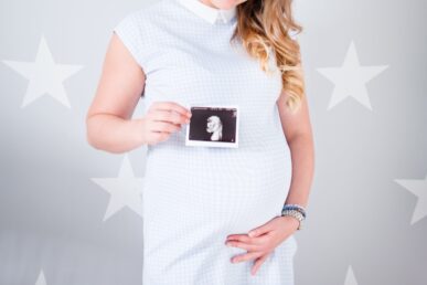 a pregnant lady in a white dress holding her belly and clutching a scan photo